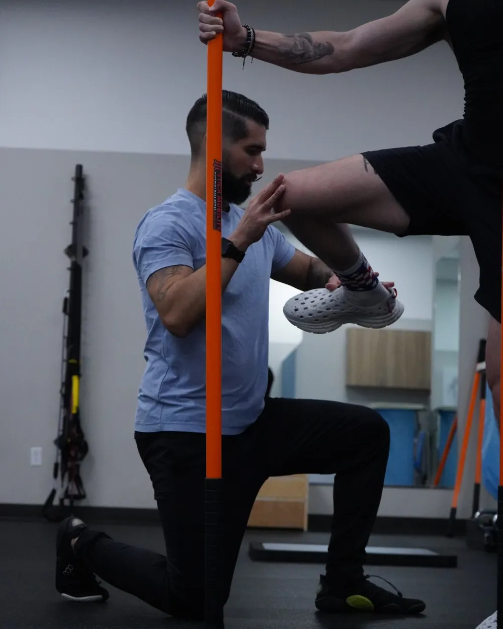 Dr. Rodriguez kneeling beside a client to assess hip and knee control as the client balances on one leg holding a mobility stick