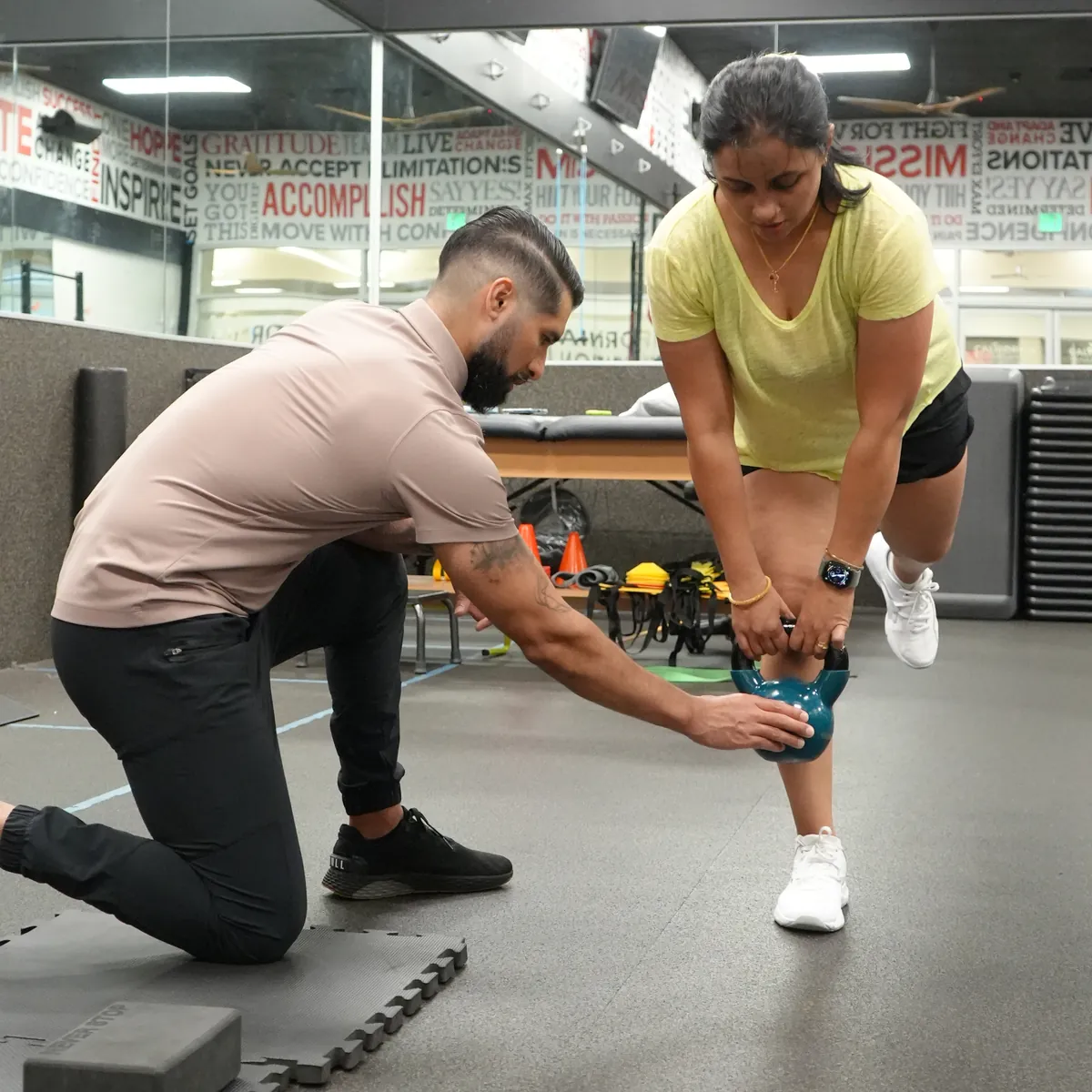 Dr. Rodriguez kneeling to guide a client's kettlebell position during a single-leg deadlift