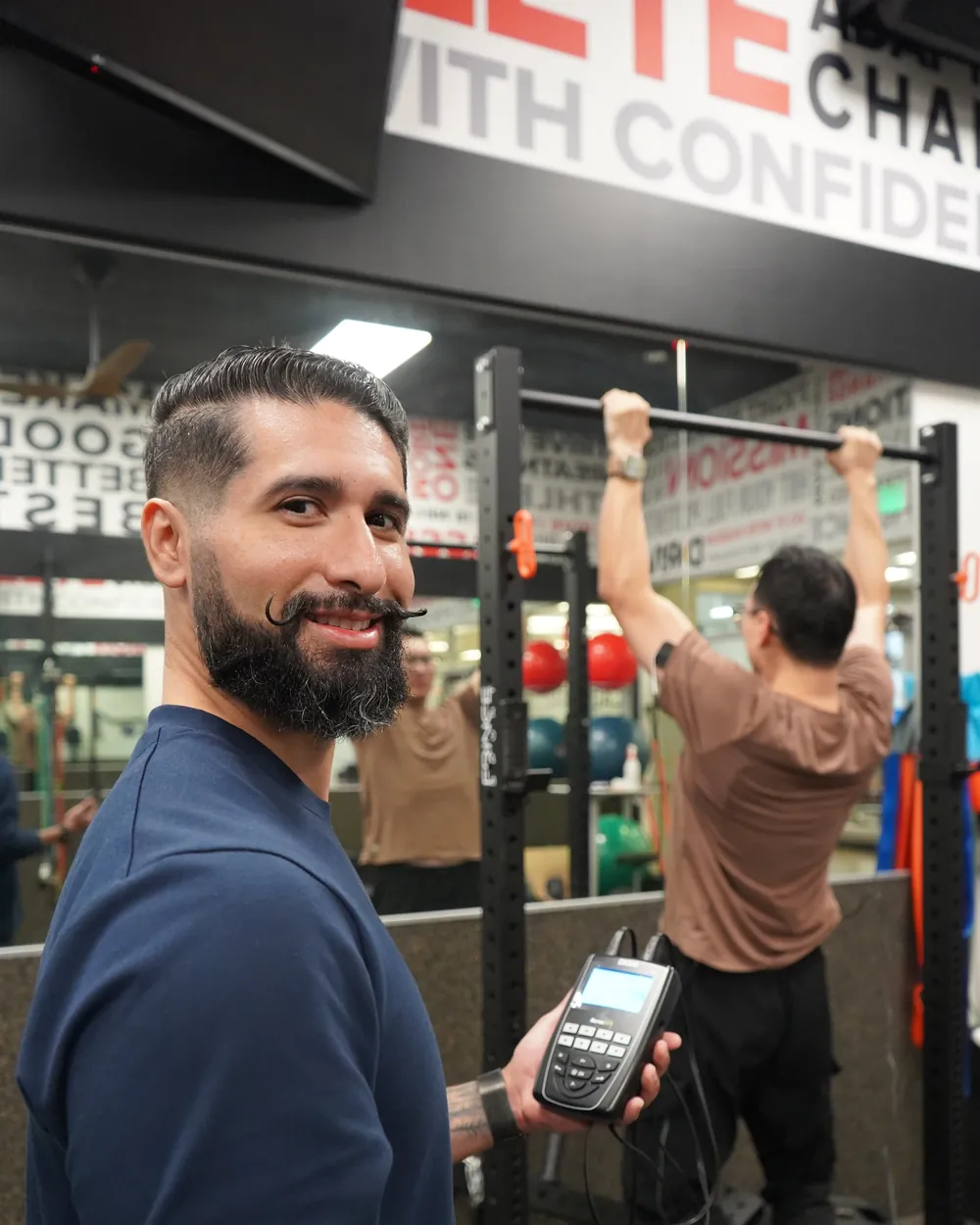 Dr. Rodriguez holding the NerveOTX DX500 while his client performs a pull-up with direct current electrodes on his arms