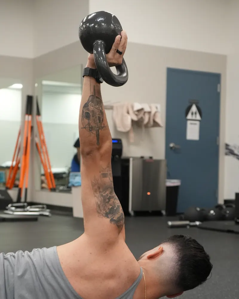 Dr. Rodriguez lying on his back holding a kettlebell overhead for shoulder stabilization