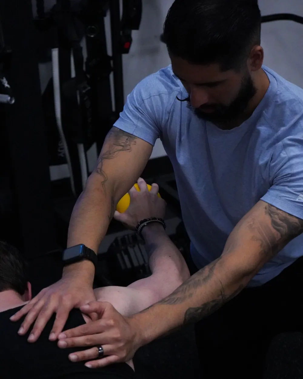 Dr. Rodriguez guiding a client's shoulder blade with both hands as the client presses a ball overhead