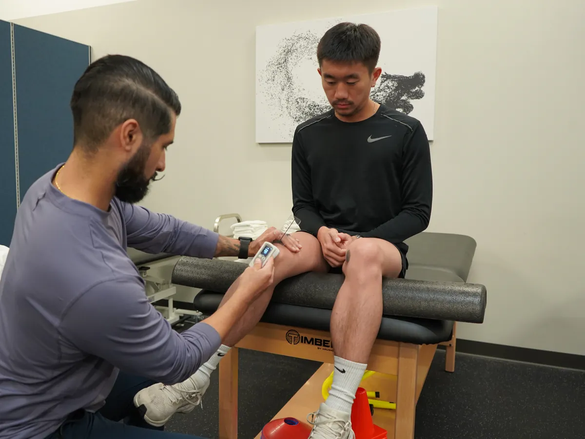 Dr. Rodriguez measuring a seated client's knee range of motion with a digital goniometer during an in-person evaluation